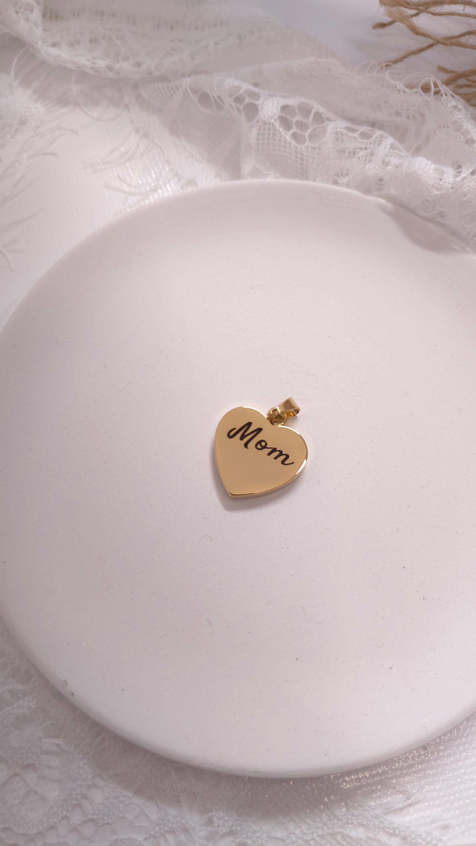 Gold heart-shaped pendant with 'Mom' engraving on a white surface